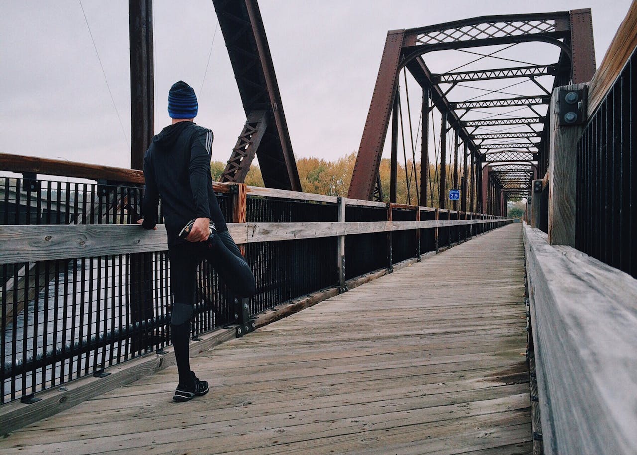 services-04 Man stretching on a wooden footbridge during a daytime run on an iron bridge, emphasizing fitness and recreation.